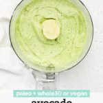 Overhead view of ingredients of avocado ranch dressing in a food processor after blending with text overlay that reads "paleo + whole30, or vegan avocado ranch dressing"