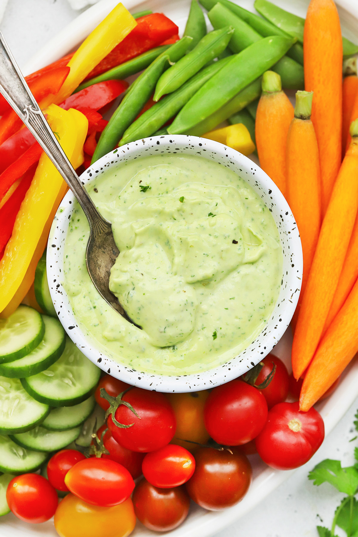 Overhead view of a bowl of avocado ranch dip with colorful fresh veggies on a white platter