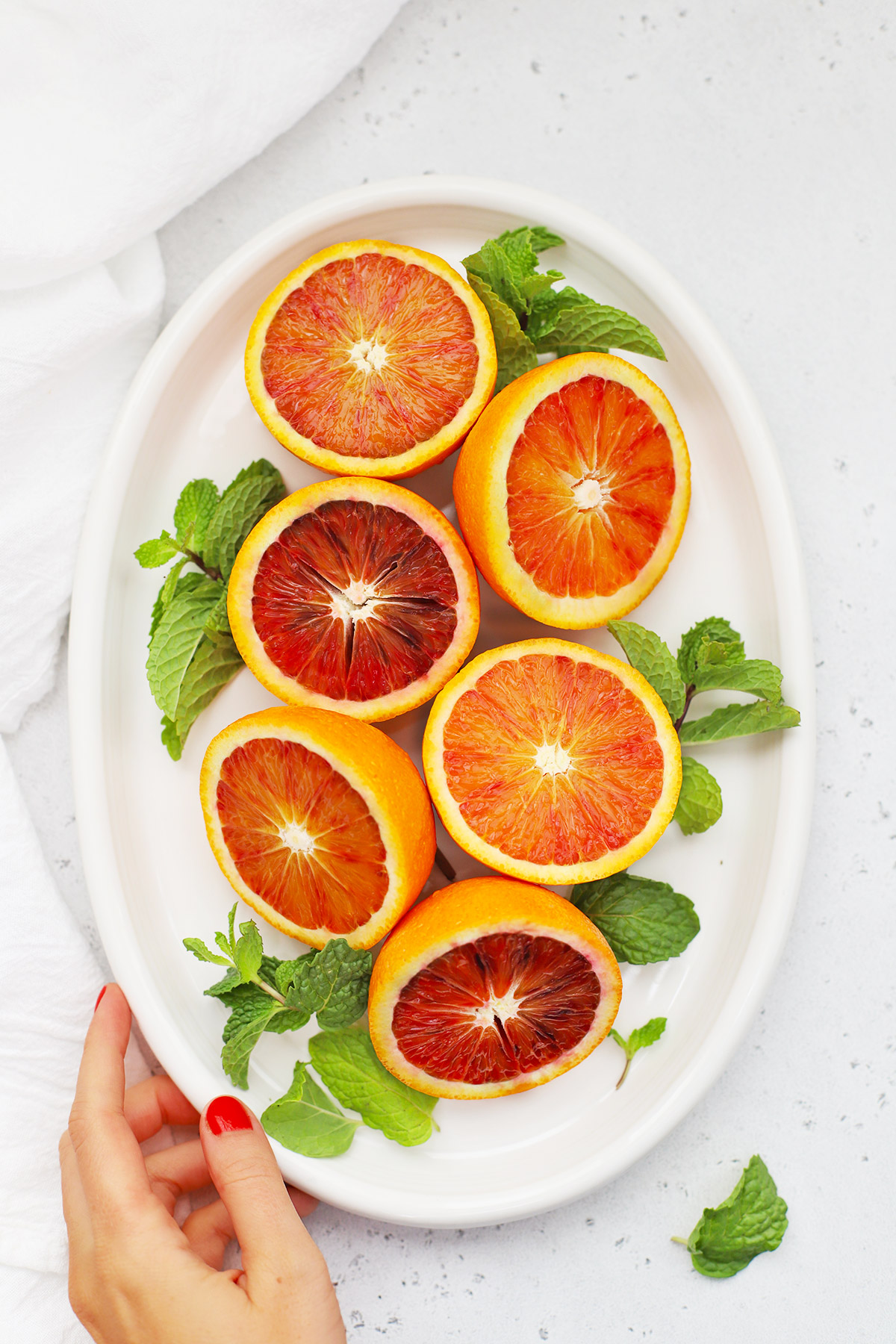 Overhead view of Halved blood oranges on a white platter with fresh mint