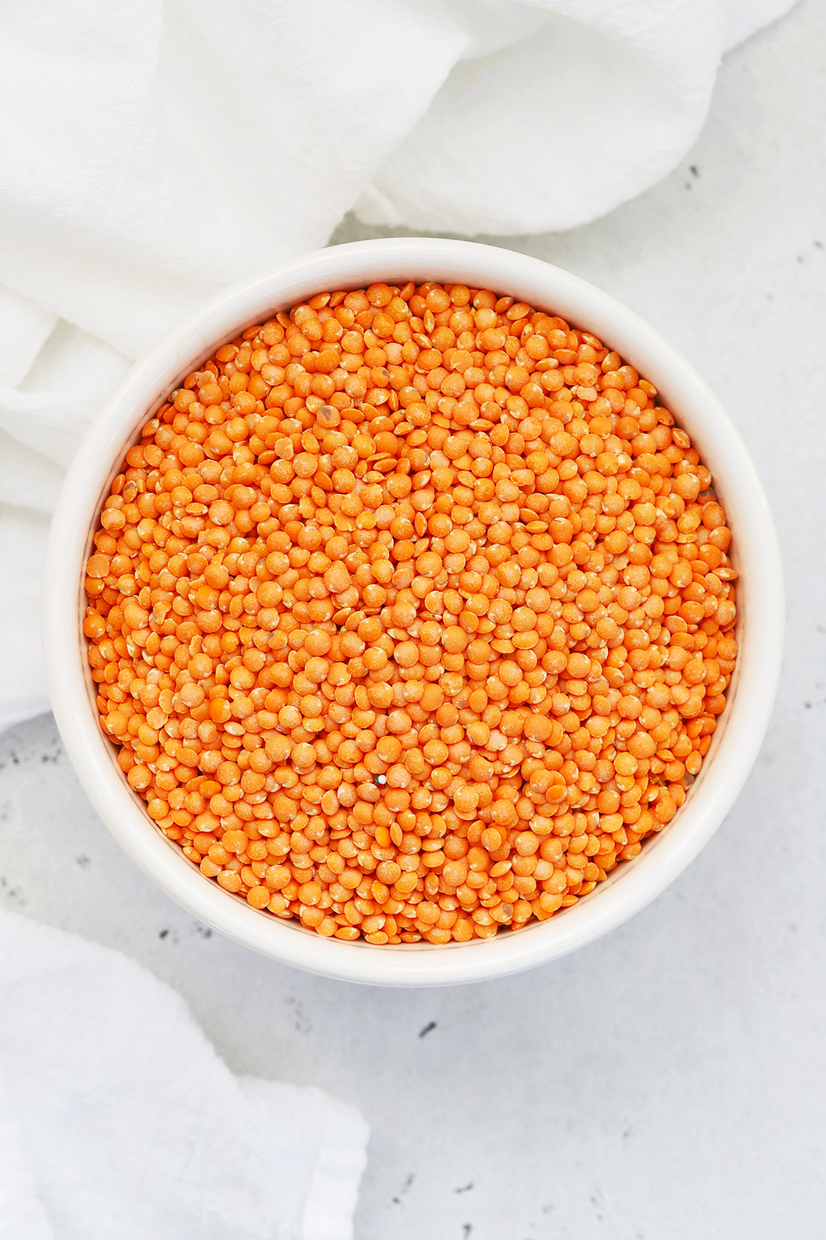 Overhead bowl of dry red lentils on a white background