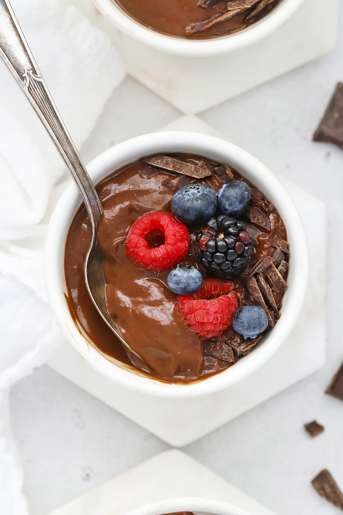 Close up overhead view of small white bowls of avocado chocolate mousse topped with fresh berries and shaved chocolate