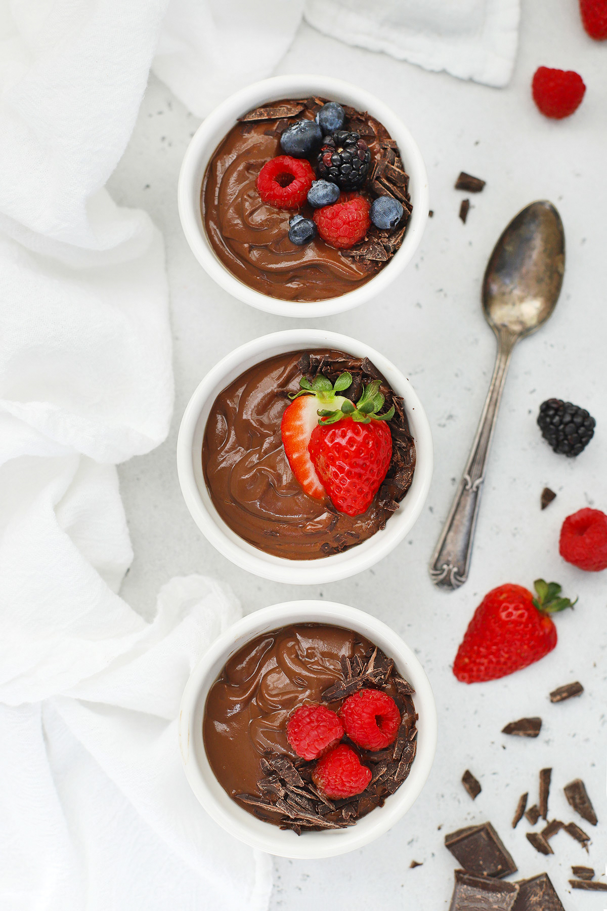 overhead view of small white bowls of avocado chocolate mousse topped with fresh berries and shaved chocolate