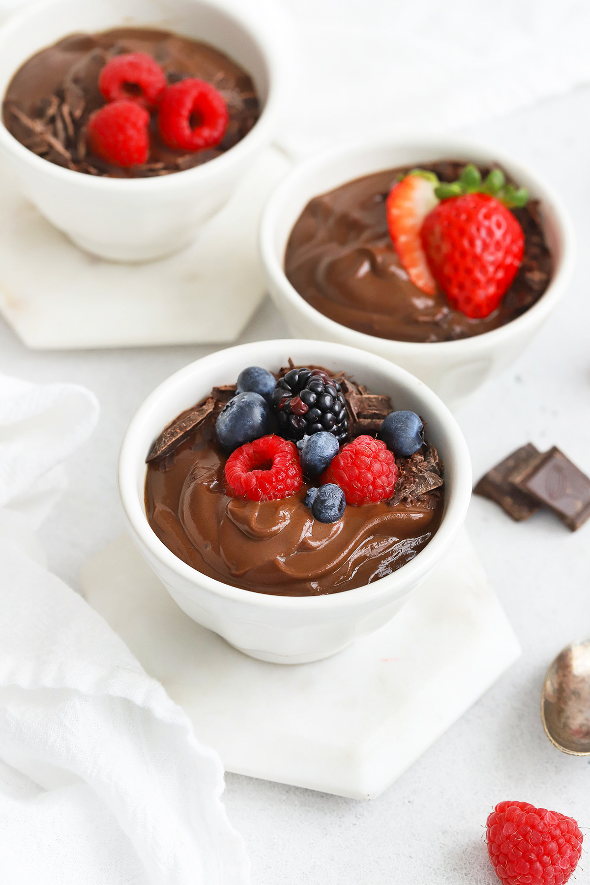 front view of small white bowls of avocado chocolate mousse topped with fresh berries and shaved chocolate