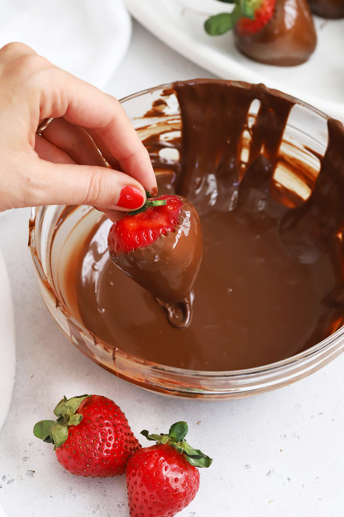 Front view of a hand dipping a strawberry into a bowl of dairy-free chocolate