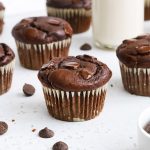 Gluten-free chocolate banana muffins on a white background with chocolate chips scattered around