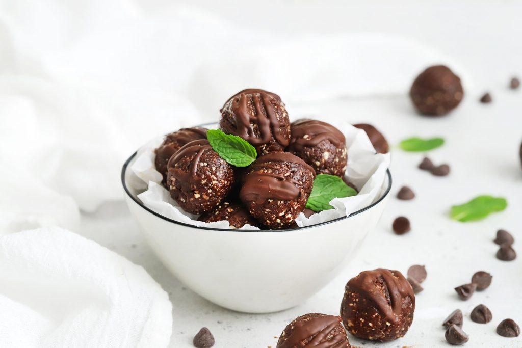 Front view of a bowl of mint chocolate energy bites with a few mint leaves.