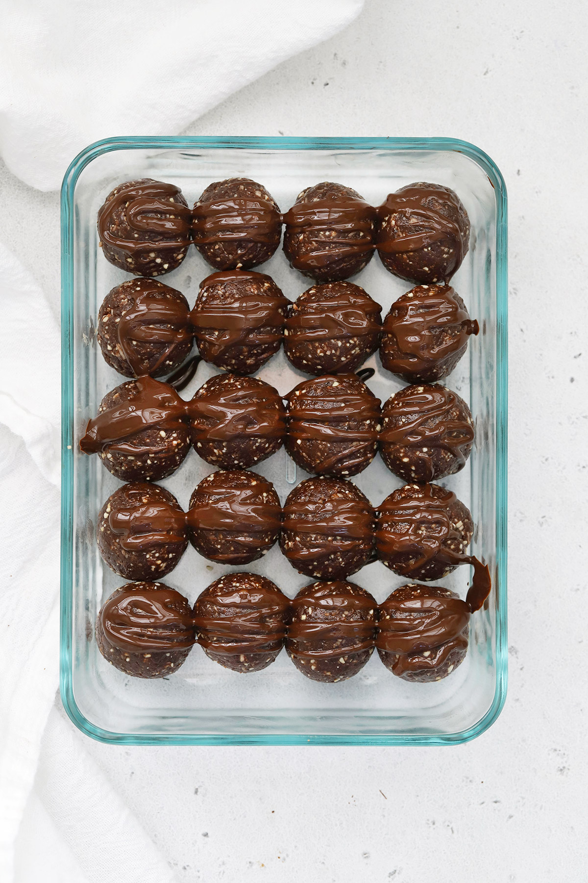 Overhead view of a glass rectangular food storage container of mint chocolate energy bites drizzled with chocolate. 