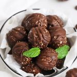 Close up Front view of a bowl of mint chocolate energy bites with a few mint leaves.