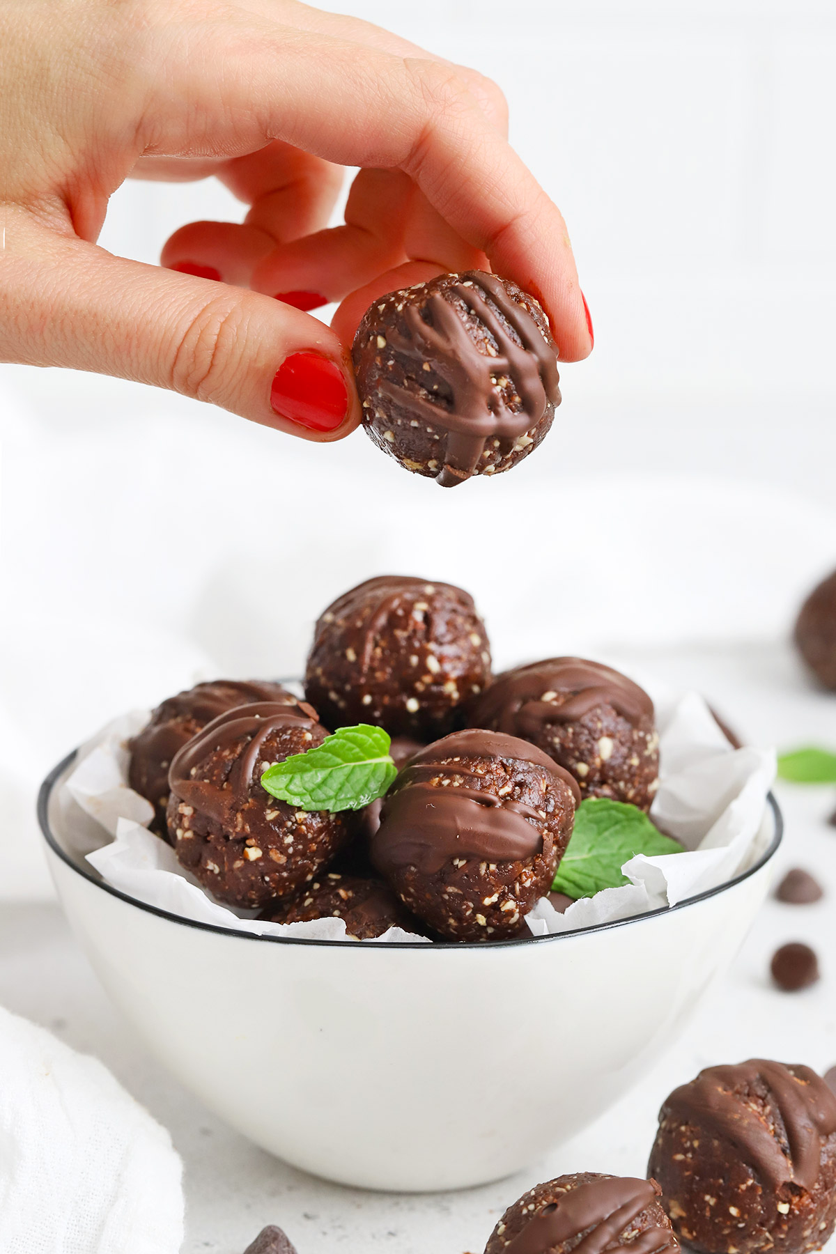 Front view of a hand taking an energy bite out of a white bowl of mint chocolate energy bites drizzled with chocolate. 