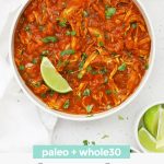 Overhead view of a bowl of Paleo Slow Cooker Butter Chicken in a white bowl topped with fresh cilantro and a lime wedge with text overlay that reads "paleo + whole30 Slow Cooker Butter Chicken"