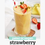 Glass of Strawberry Orange Sunrise Smoothie topped with fresh pineapple and strawberries with a red and white stripe straw with text overlay that reads "paleo or vegan Strawberry Orange Sunrise Smoothie"
