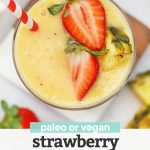Close up view of Glass of Strawberry Orange Sunrise Smoothie topped with fresh pineapple and strawberries with a red and white stripe straw with text overlay that reads "paleo or vegan Strawberry Orange Sunrise Smoothie"