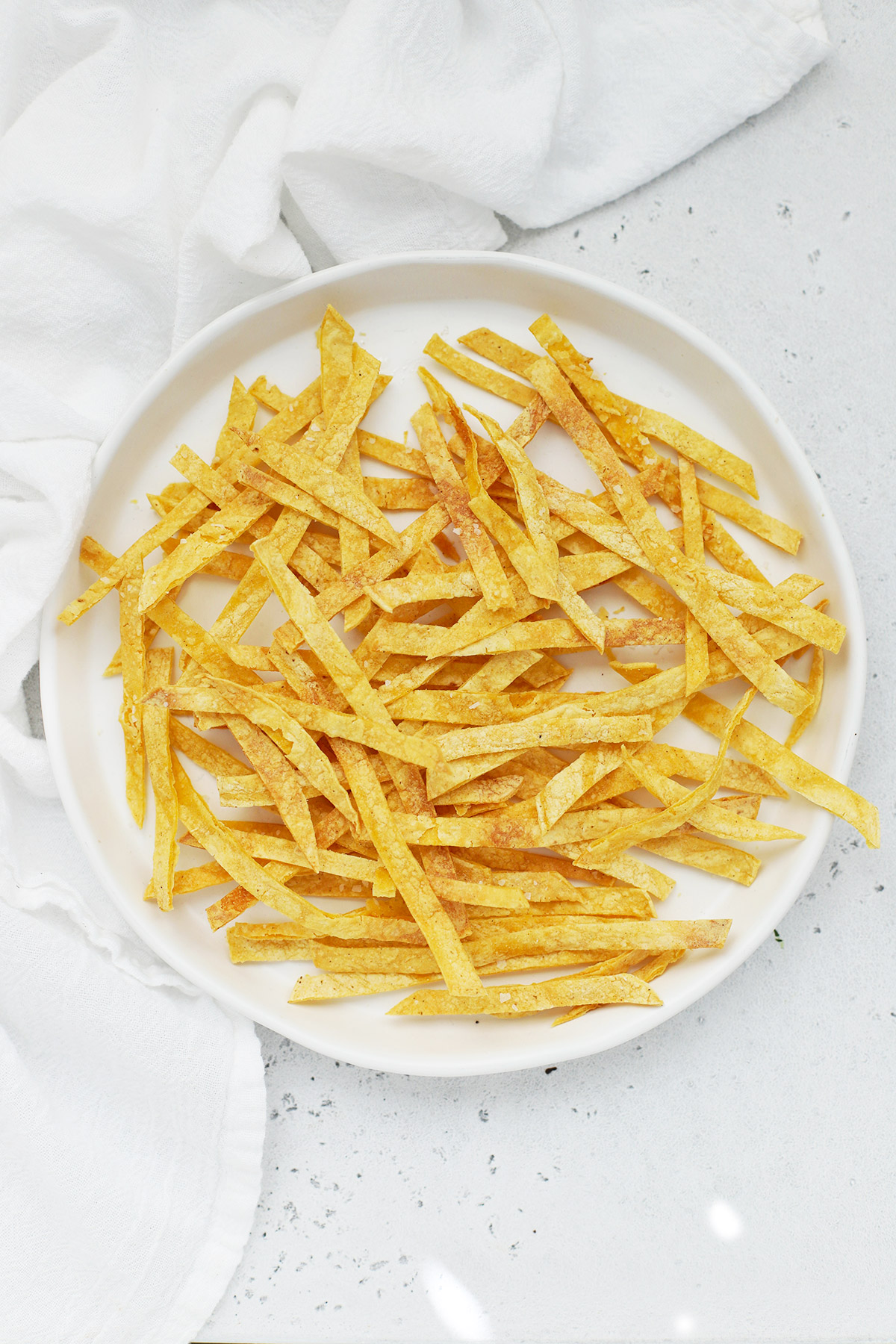 Overhead view of a plate of crispy baked tortilla strips on a white background