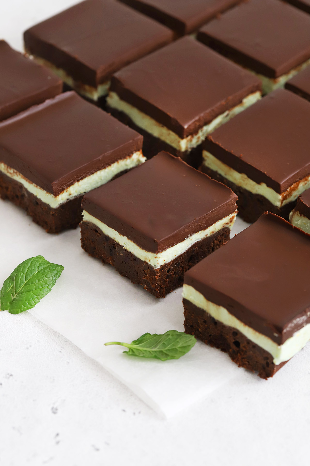 Overhead view of gluten-free mint brownie squares on a white background with fresh mint leaves scattered around