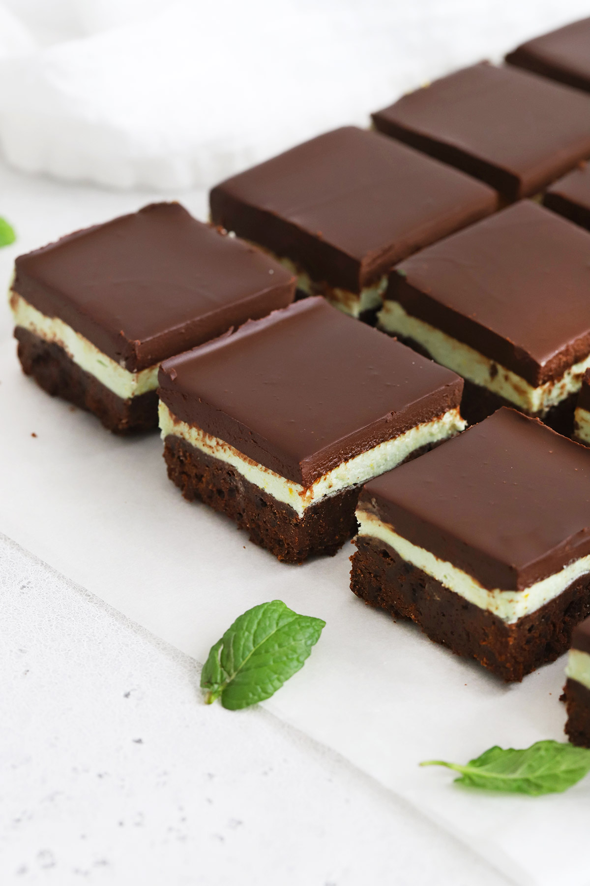 Overhead view of gluten-free mint brownie squares on a white background with fresh mint leaves scattered around