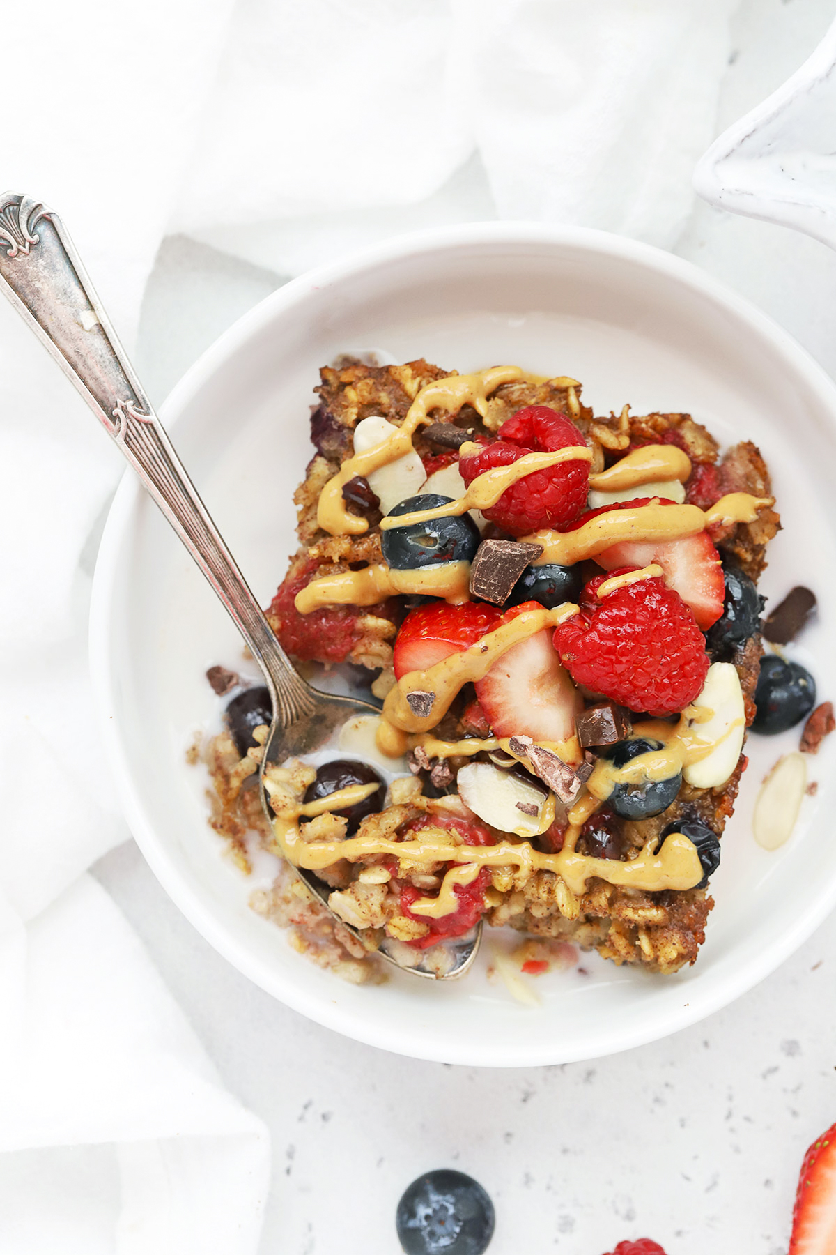 Overhead view of a slice of mixed berry baked oatmeal topped with peanut butter, sliced almonds, fresh berries, and cacao nibs
