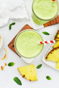 Close up overhead view of pineapple mint smoothie in a glass with a red striped straw
