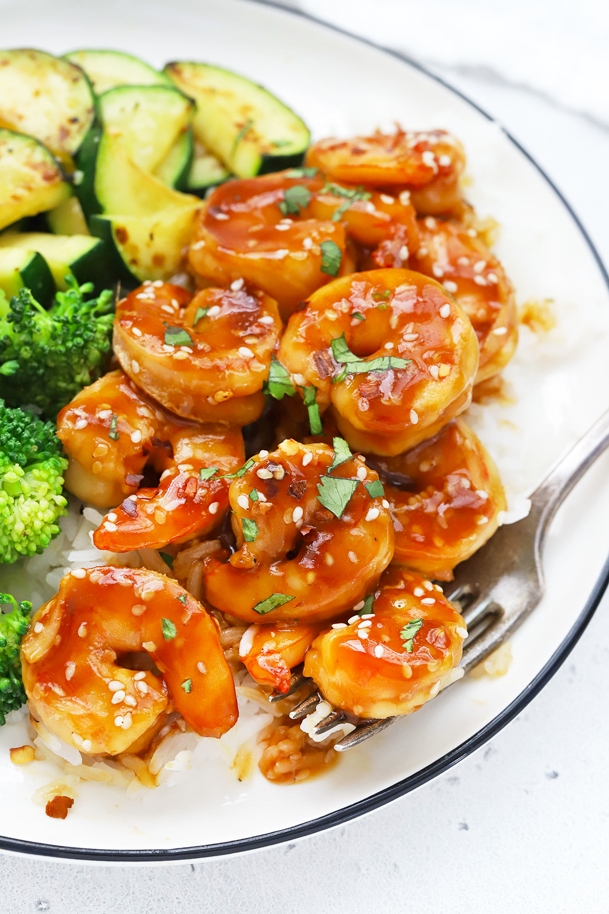 Close up Overhead view of a plate of easy sesame shrimp with broccoli and zucchini on a white background