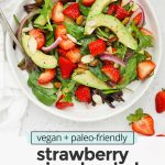 Overhead view of strawberry spinach salad on a white salad plate with text overlay that reads "vegan + paleo-friendly strawberry spinach salad: fresh + light + bright"