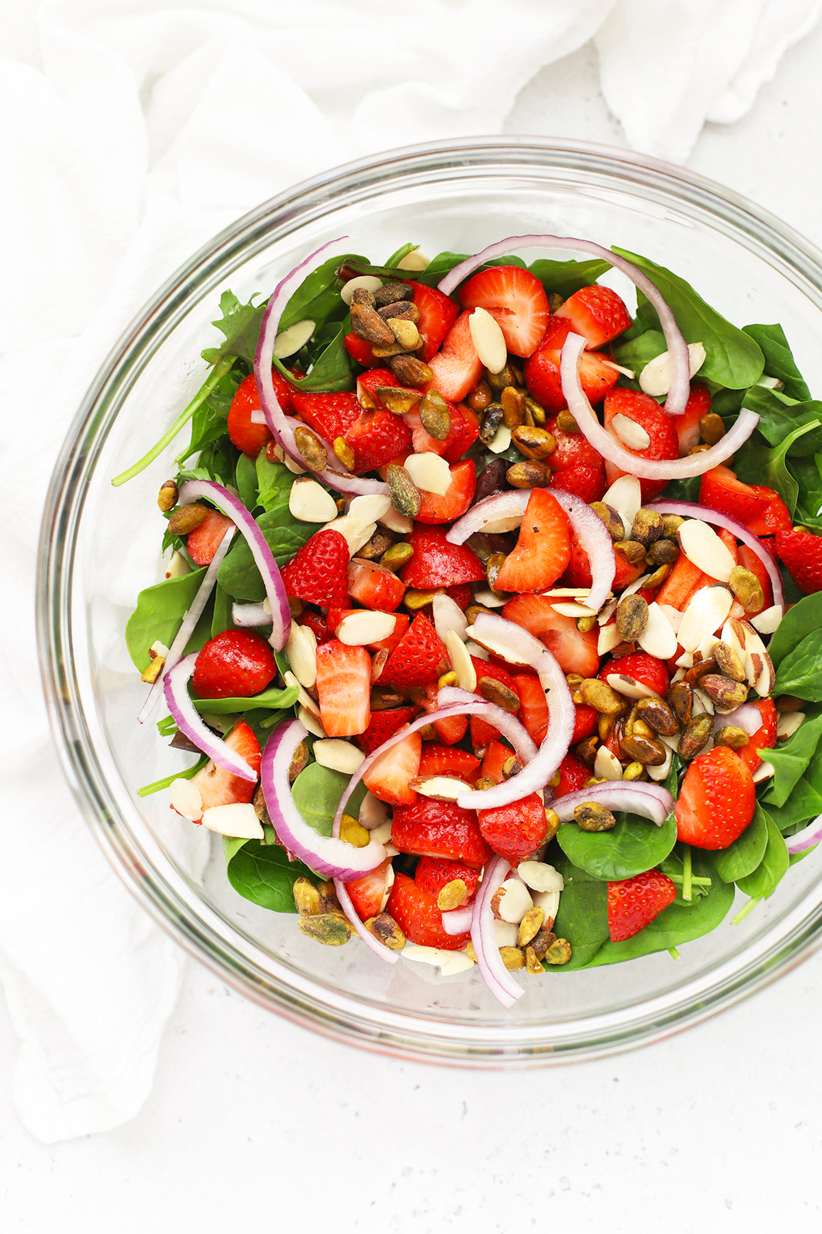 Overhead view of a mixing bowl of strawberry spinach salad ready to be tossed with dressing