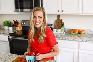 Emily Dixon from One Lovely Life in a red dress standing in her kitchen with fresh berries