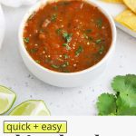 Front view of a bowl of chipotle salsa with a platter of tortilla chips on a white background with text overlay that reads "quick + easy chipotle salsa: smoky + flavorfu; + delicious"