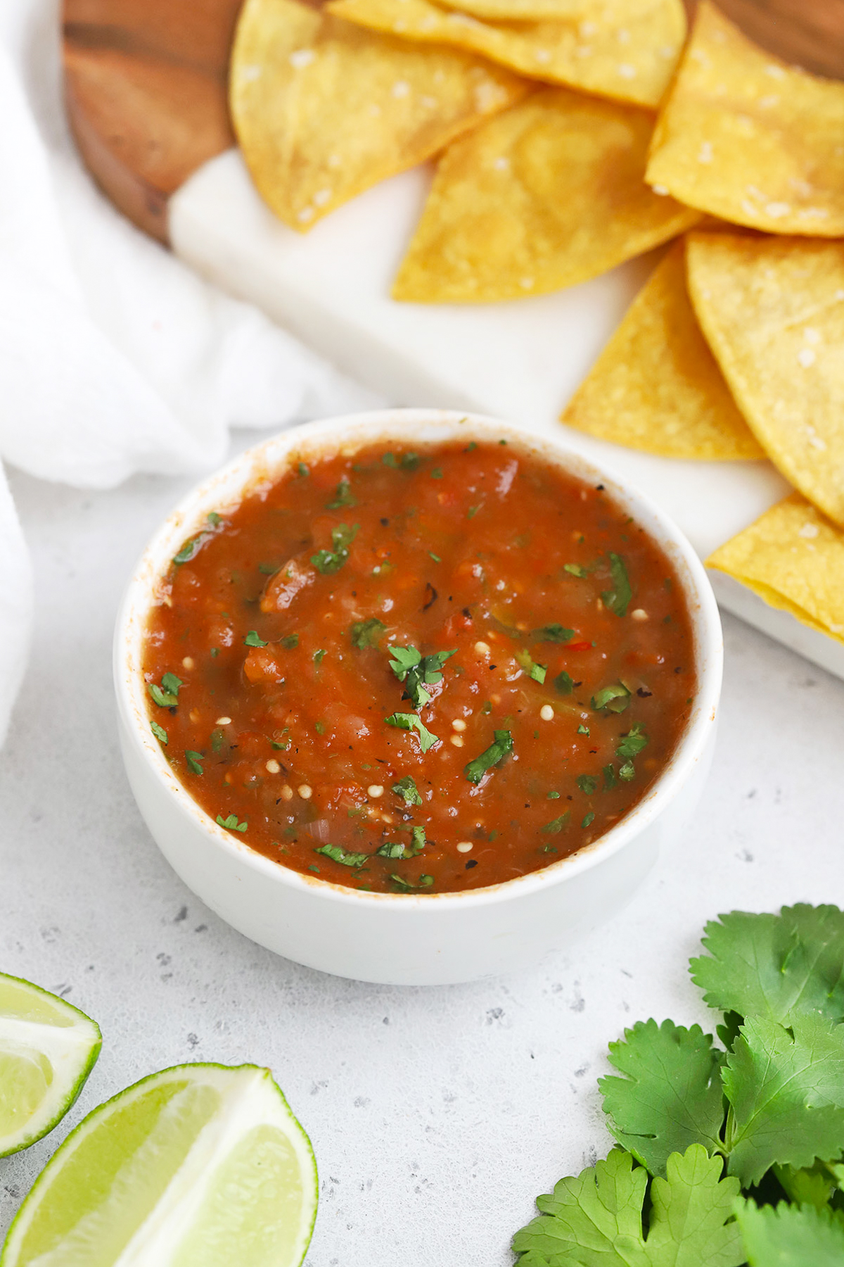 Front view of a bowl of chipotle salsa with a platter of tortilla chips on a white background