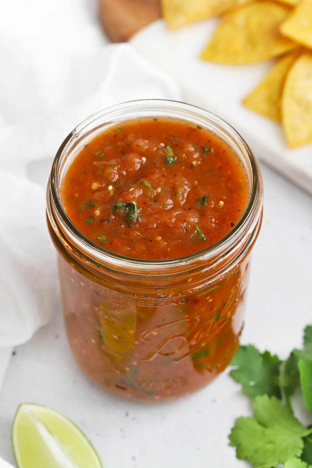 Front view of a jar of chipotle salsa with a platter of tortilla chips on a white background