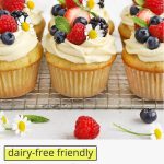 Front view of gluten-free lemon cupcakes with lemon frosting, fresh berries, and edible flowers on a white background with text overlay that reads "dairy-free friendly gluten-free lemon cupcakes"