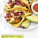 Front view of three honey lime chicken tacos with slaw on a white plate with text overlay that reads "gluten-free + easy honey lime chicken tacos: fresh + flavorful + fun"