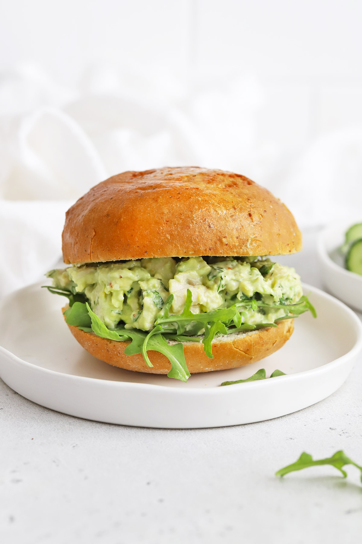 Front view of an avocado chicken salad sandwich with arugula on a white plate.