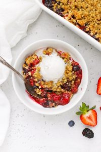 Overhead view of a bowl of gluten-free mixed berry crisp topped with dairy-free vanilla ice cream on a white background