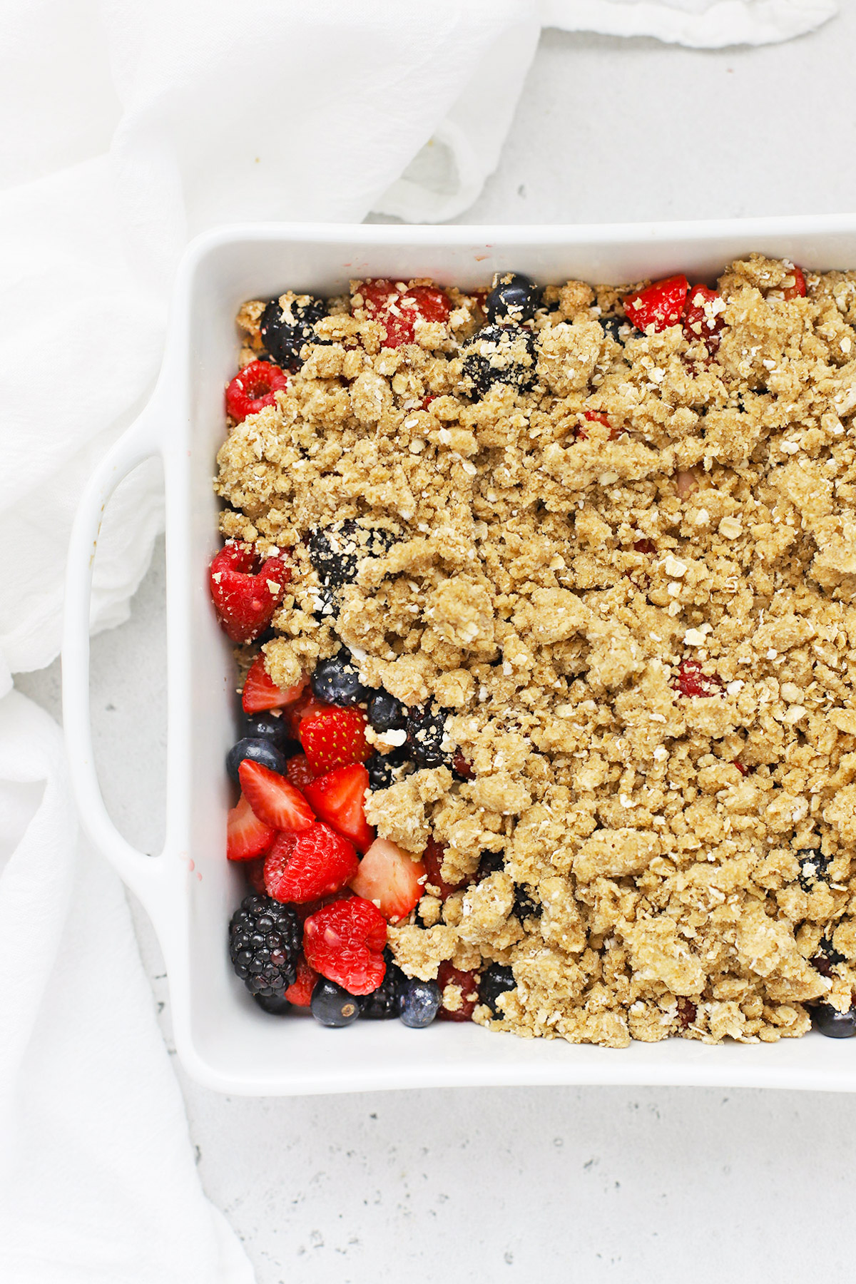 Overhead view of gluten-free crumble topping being added to a mixed berry crisp filling