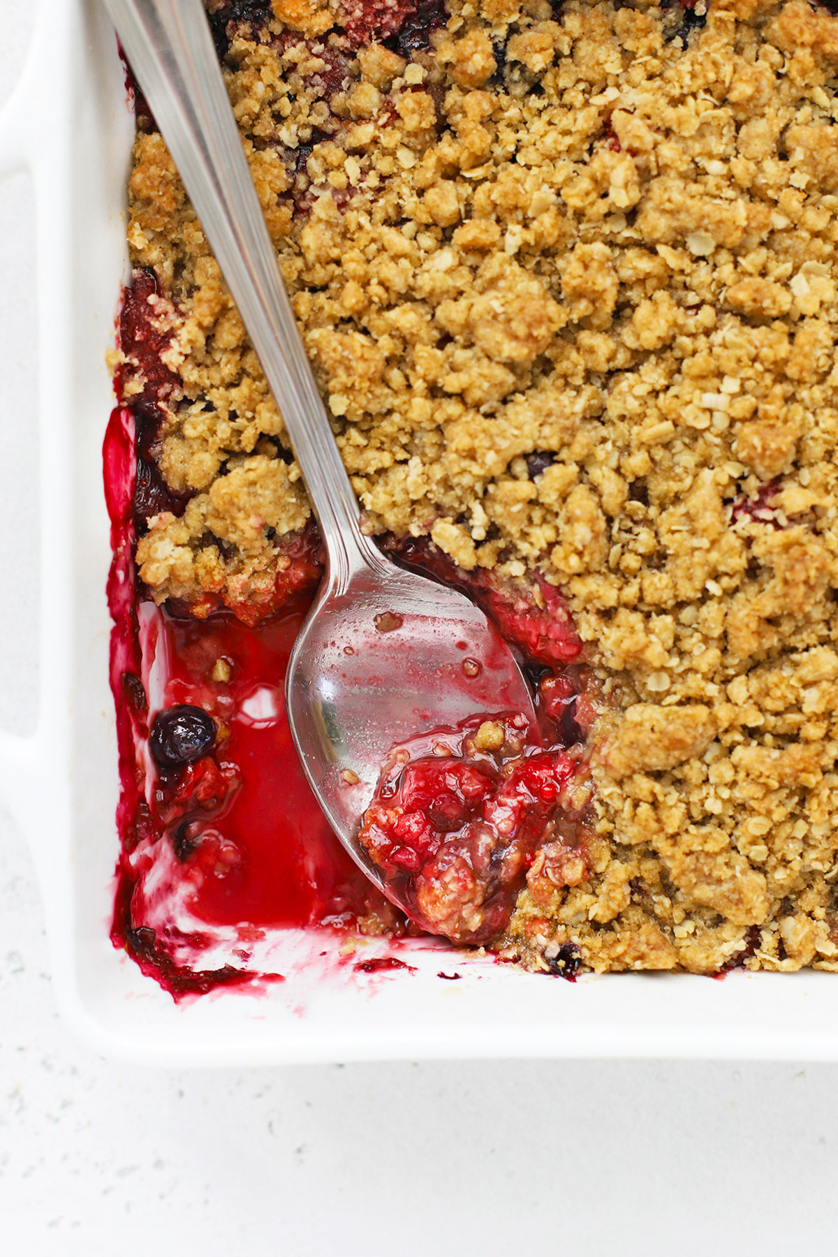 Overhead view of a baking dish of gluten-free berry crisp with a serving spoon