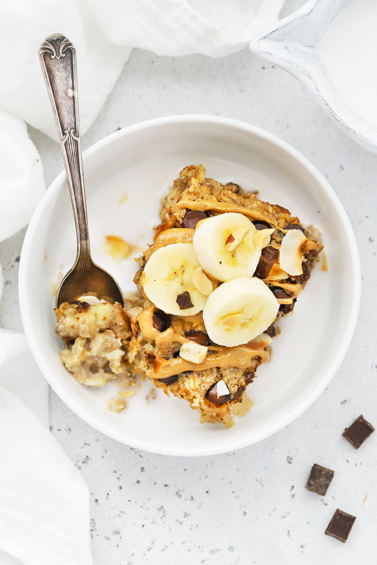Overhead view of a bowl of Chunky Monkey Baked Oatmeal topped with bananas, drizzled peanut butter, and milk.