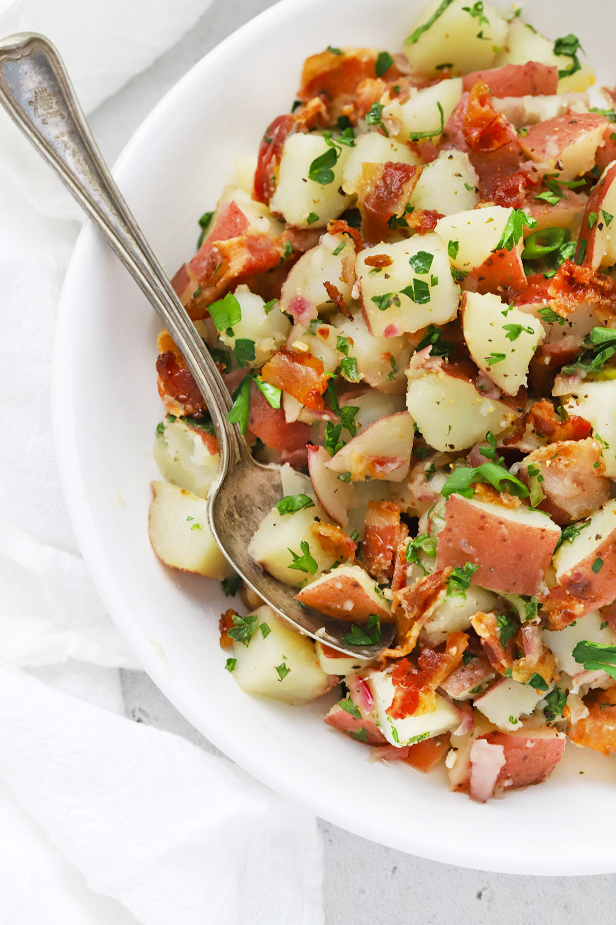 Close up front view of a white bowl of German Potato Salad with Bacon Dressing
