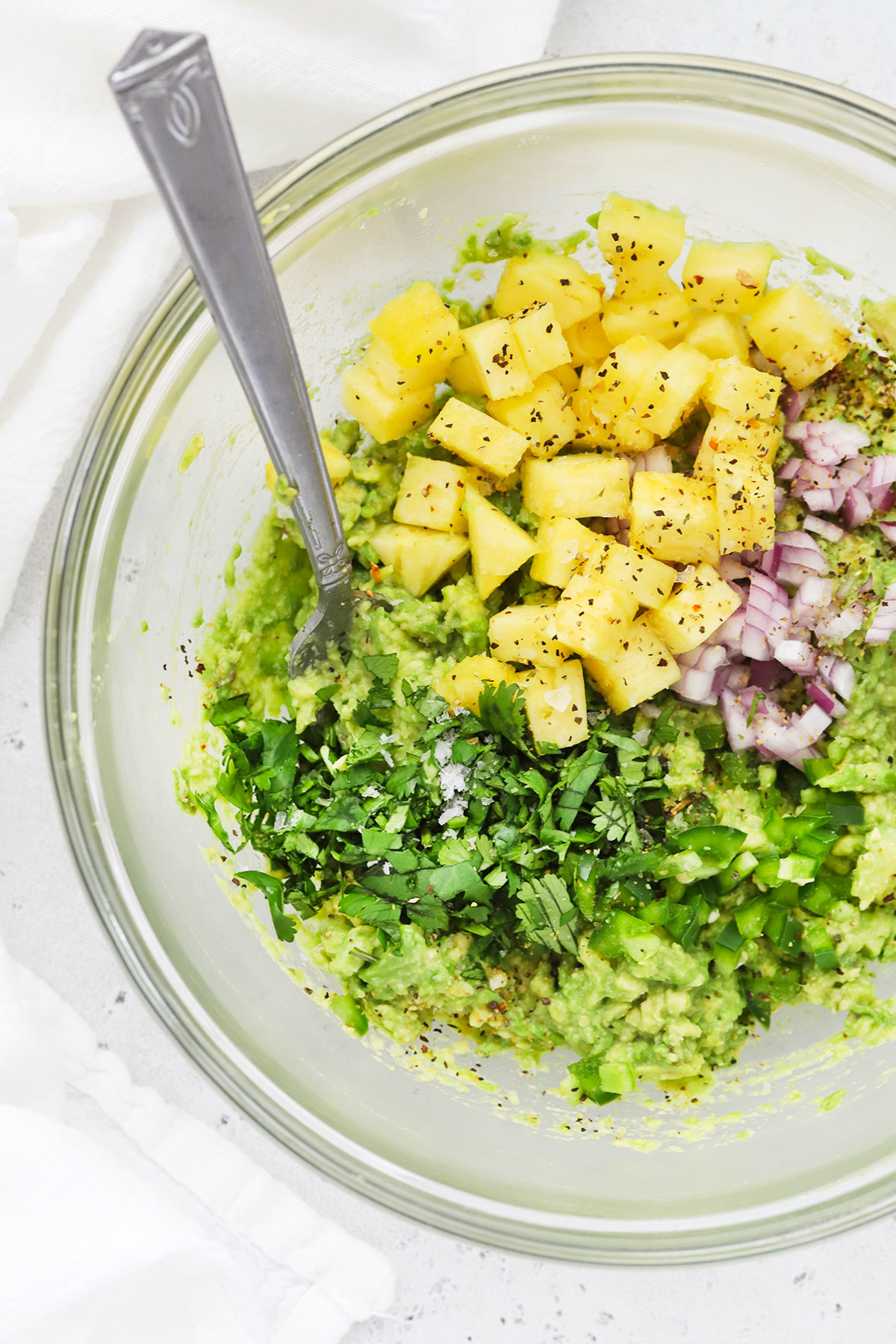 Overhead view of a glass bowl with ingredients for pineapple guacamole inside