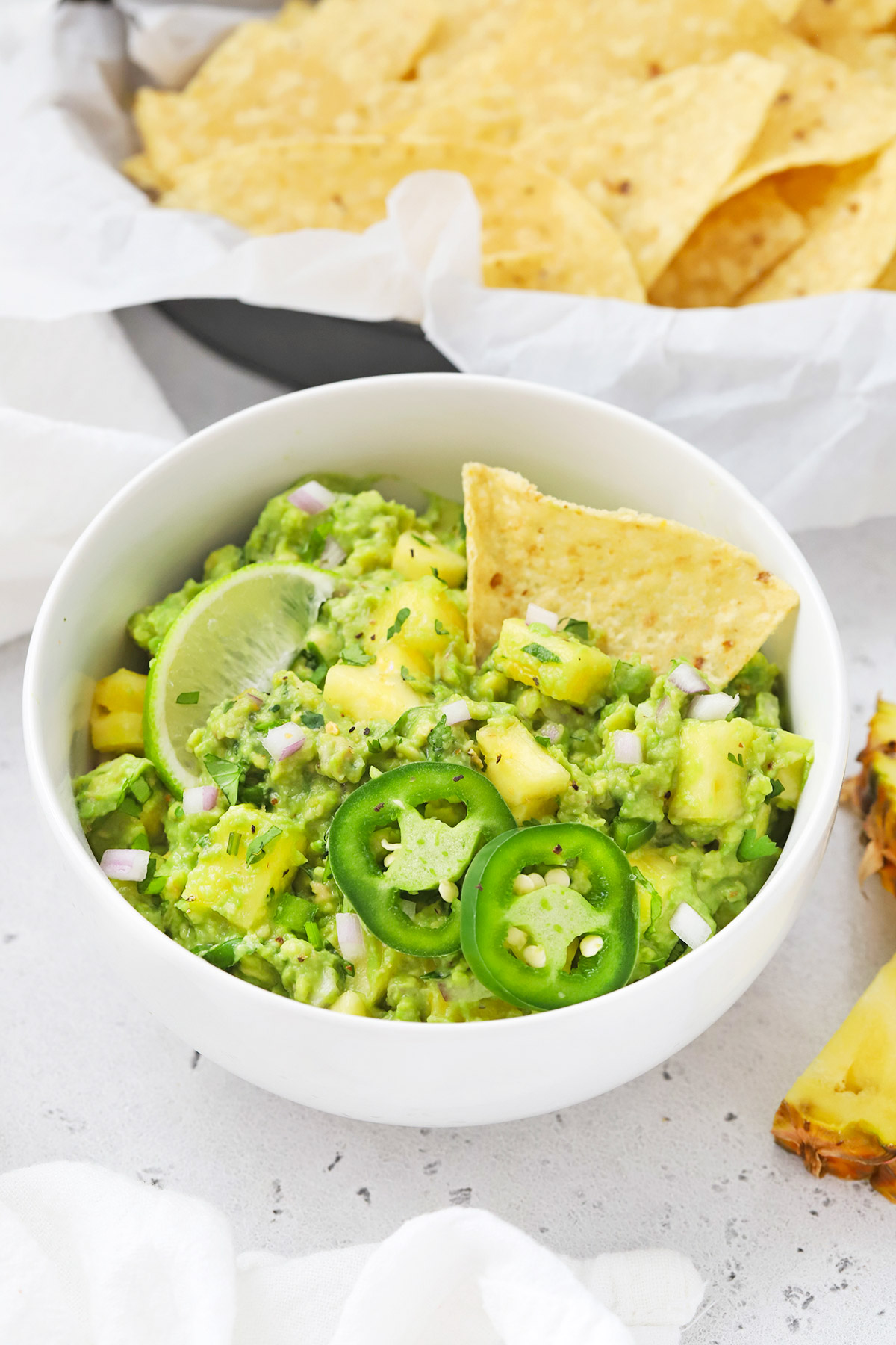 Front view of a bowl of pineapple guacamole with a chip dipped inside