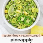 Close up overhead view of a bowl of pineapple guacamole with a chip dipped inside with text overlay that reads "gluten-free + vegan + paleo pineapple guacamole: sweet + spicy + savory"