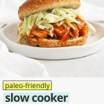 Front view of a slow cooker BBQ chicken sandwich on a white background with text overlay that reads " Paleo-Friendly Slow Cooker BBQ Chicken: Easy + Great For a Crowd!"