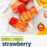 Overhead view of strawberry orange sunrise popsicles on a platter of ice with text overlay that reads "paleo & vegan Strawberry Orange Sunrise Popsicles: Easy + Healthy + Fresh"