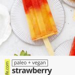 Overhead view of a strawberry orange sunrise popsicle on a circular coaster with text overlay that reads "paleo & vegan Strawberry Orange Sunrise Popsicles: Easy + Healthy + Fresh"