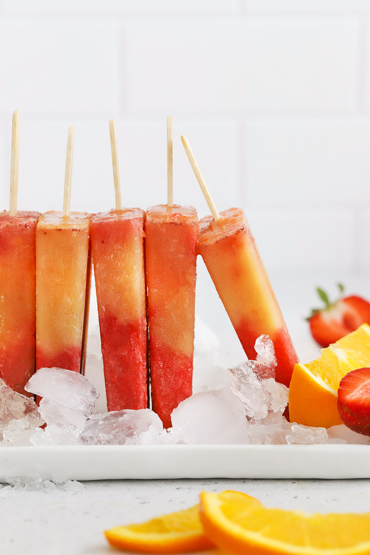 Front view of strawberry orange sunrise popsicles standing up in ice