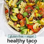 Overhead view of a speckled bowl of healthy taco pasta salad on a white background with text overlay that reads "gluten-free + vegan healthy taco pasta salad with chili lime dressing"