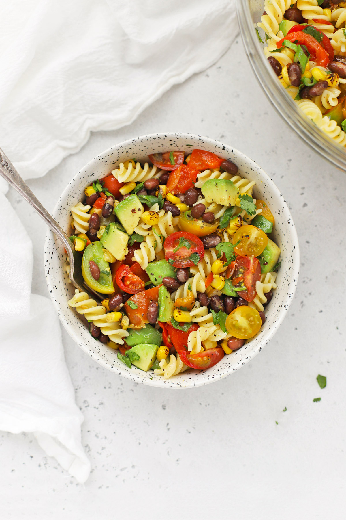 Overhead view of a speckled bowl of healthy taco pasta salad on a white background