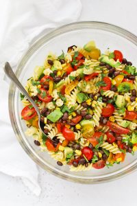 Overhead view of a glass mixing bowl of healthy taco pasta salad on a white background