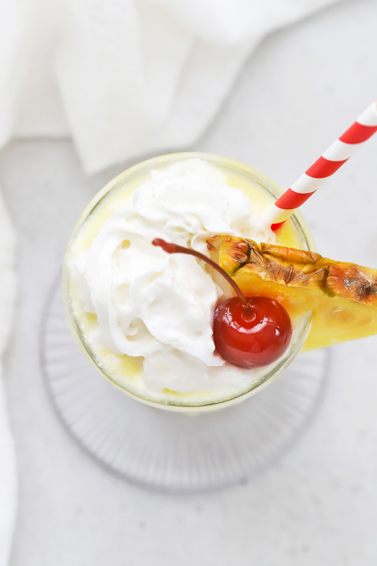 Close up overhead view of a virgin pina colada with whipped cream and a cherry on a white background