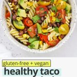 Overhead view of a speckled bowl of healthy taco pasta salad on a white background with text overlay that reads "healthy gluten-free + vegan taco pasta salad with chili lime dressing: quick + healthy + fresh"
