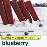 Front view of homemade blueberry pomegranate popsicles standing upright on a platter of ice with text overlay that reads "paleo + vegan + healthy blueberry pomegranate popsicles: refreshing + simple + delicious!"