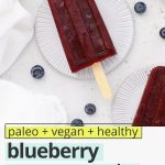 Overhead view of healthy blueberry pomegranate popsicles on coasters with fresh blueberries scattered around with text overlay that reads "paleo + vegan + healthy blueberry pomegranate popsicles: refreshing + simple + delicious!"